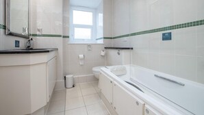 Een badkamer met toilet, wastafel en bad. Er is een raam boven het toilet en een prullenbak is te zien.
