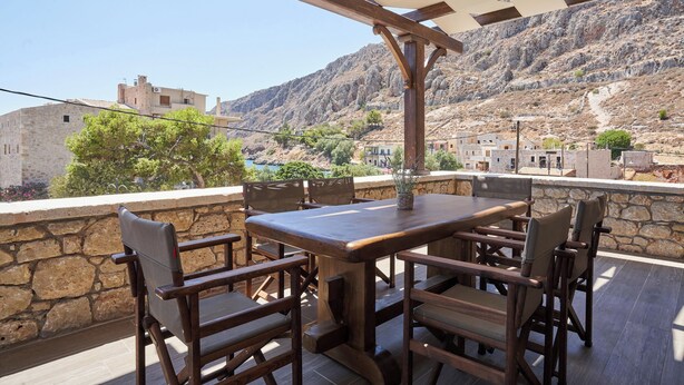 Ein Holztisch mit Stühlen auf einer Terrasses mit Steinmauer und Blick auf eine gebirgige Landschaft.