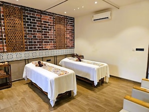 A room with two beds, a brick wall, a decorative screen, and an air conditioning unit.