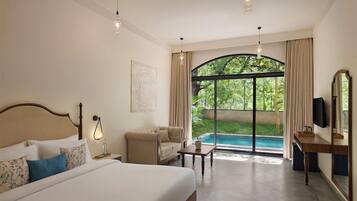 A hotel room with a bed, a sofa, a table, a TV, and a view of a swimming pool.