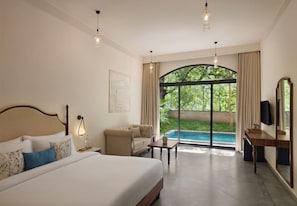 A hotel room with a bed, a sofa, a table, a TV, and a view of a swimming pool.