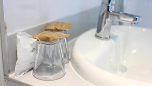 A bathroom sink with a clear glass container and a white bag on the counter. - Deluxe Double Room with View (Cardiff)
