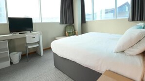 A hotel room with a bed, a desk with a chair, a television, and large windows. - Deluxe Double Room with View (Cardiff)