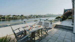 A terrace with a table set for dining, overlooking a river with boats.