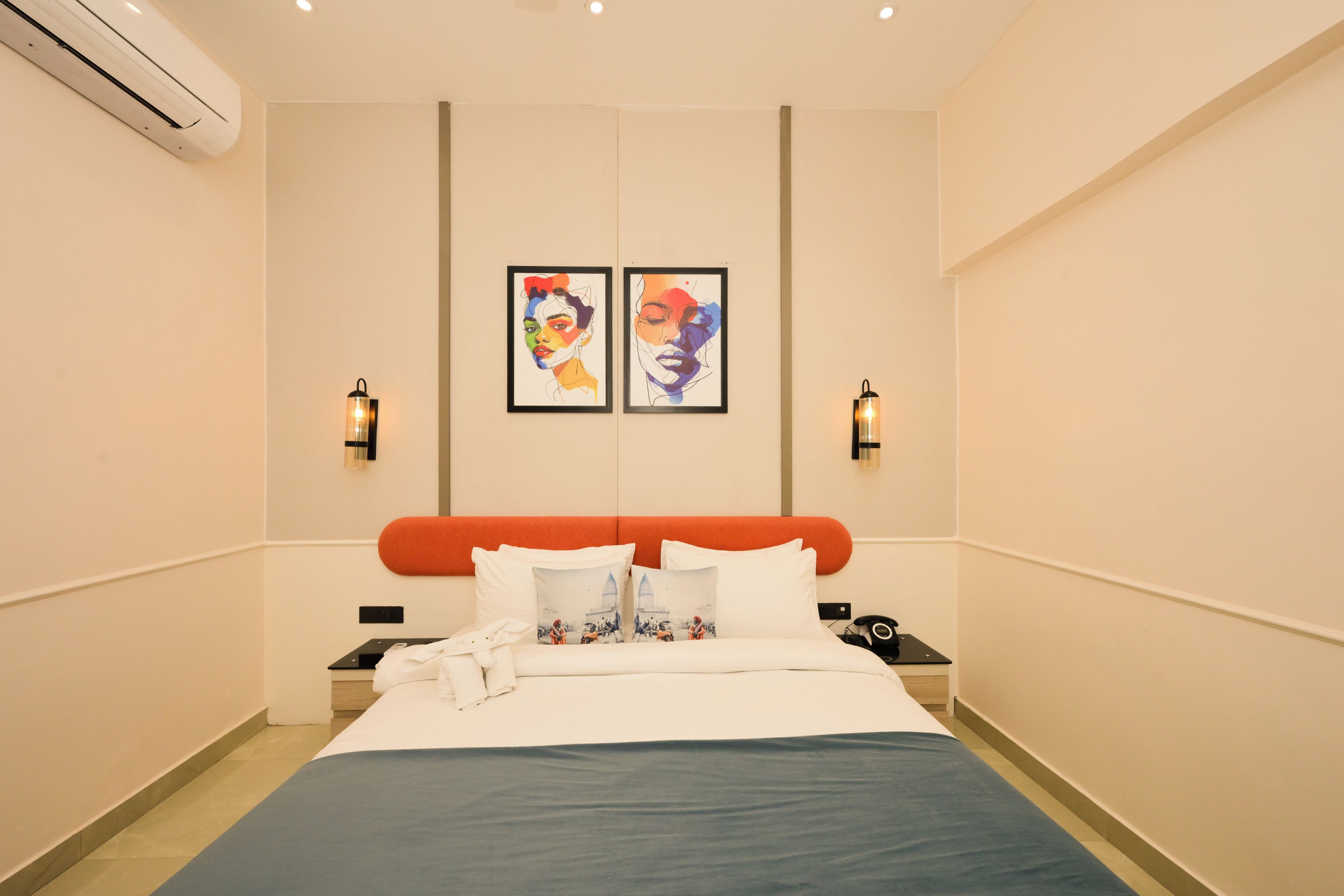 A hotel room with a bed, two wall-mounted lamps, and two framed artworks.