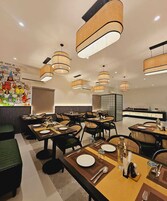 A modern dining area with multiple tables, wicker chairs, and contemporary pendant lighting.