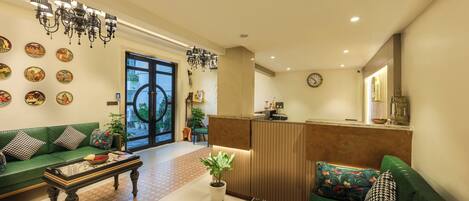 A hotel lobby with a reception desk, green sofas, a coffee table, and decorative wall art.