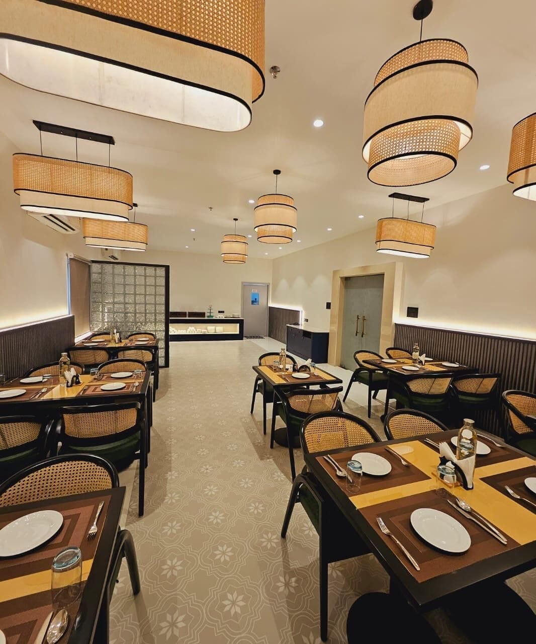 A restaurant with multiple dining tables, wicker chairs, and hanging rattan lamps.