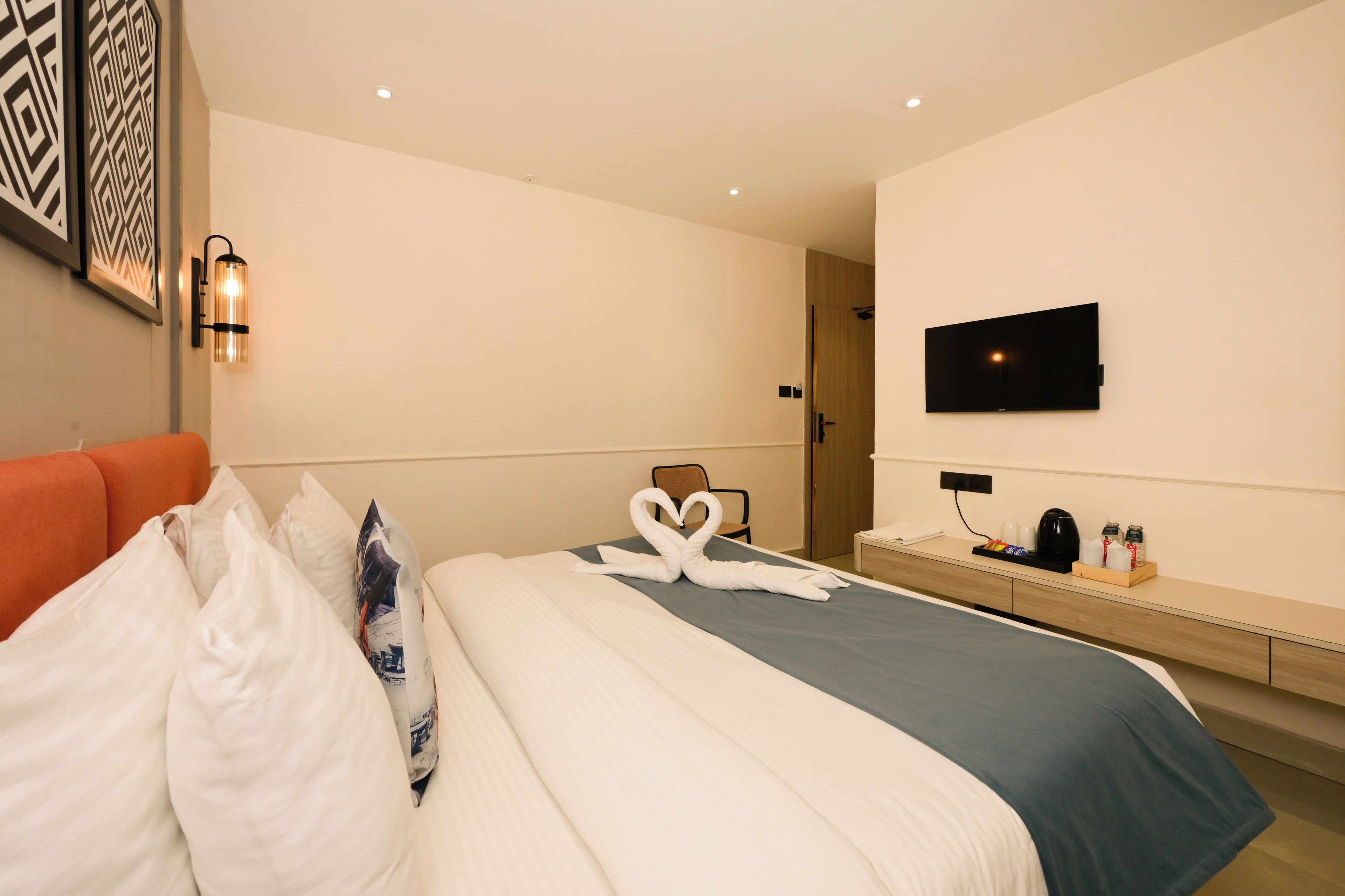 A hotel room with a bed, a TV mounted on the wall, and a desk with a coffee maker and other items.
