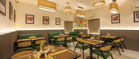 A restaurant with multiple dining tables, green upholstered booths, and hanging wicker lamps.