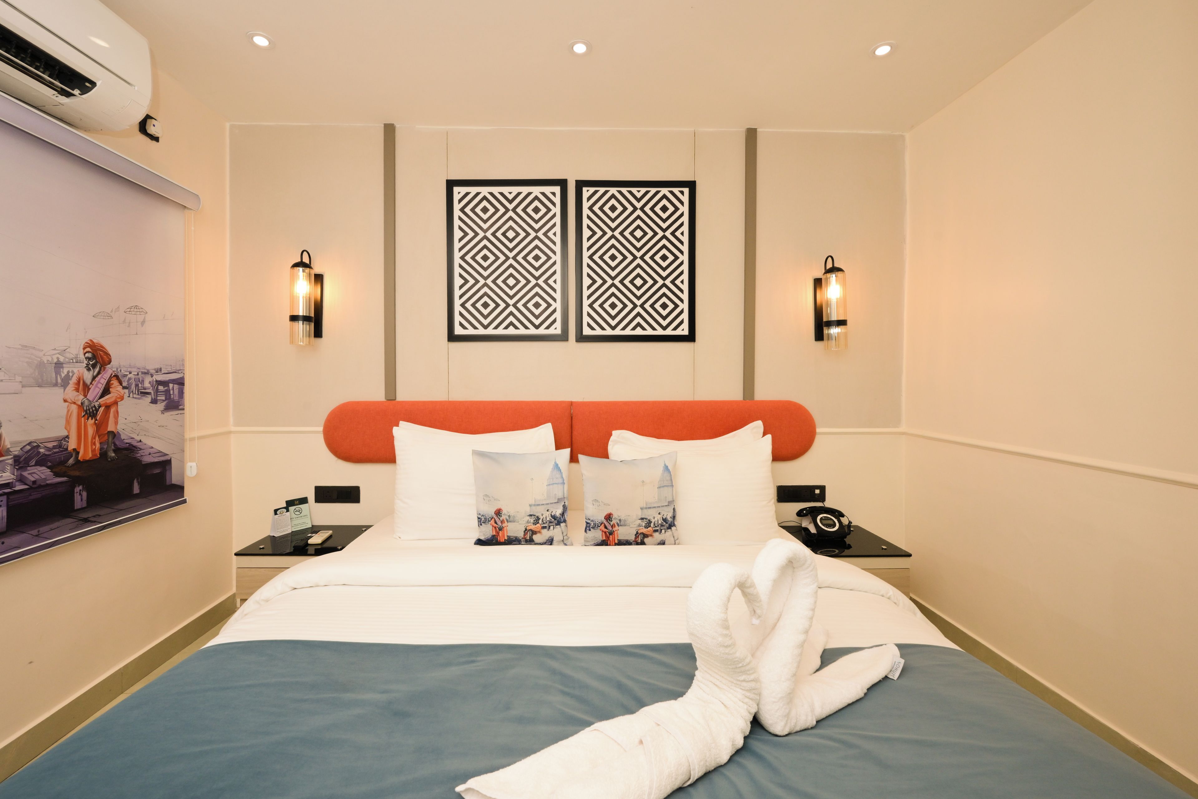 Una camera d'albergo con un letto, cuscini, un comodino, un condizionatore d'aria a parete e pannelli decorativi.