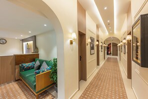A hotel hallway with a sofa, a clock, and a patterned carpet. - HERITAGE KASHINAAMA EK KAHANI BANARAS KI (Varanasi)