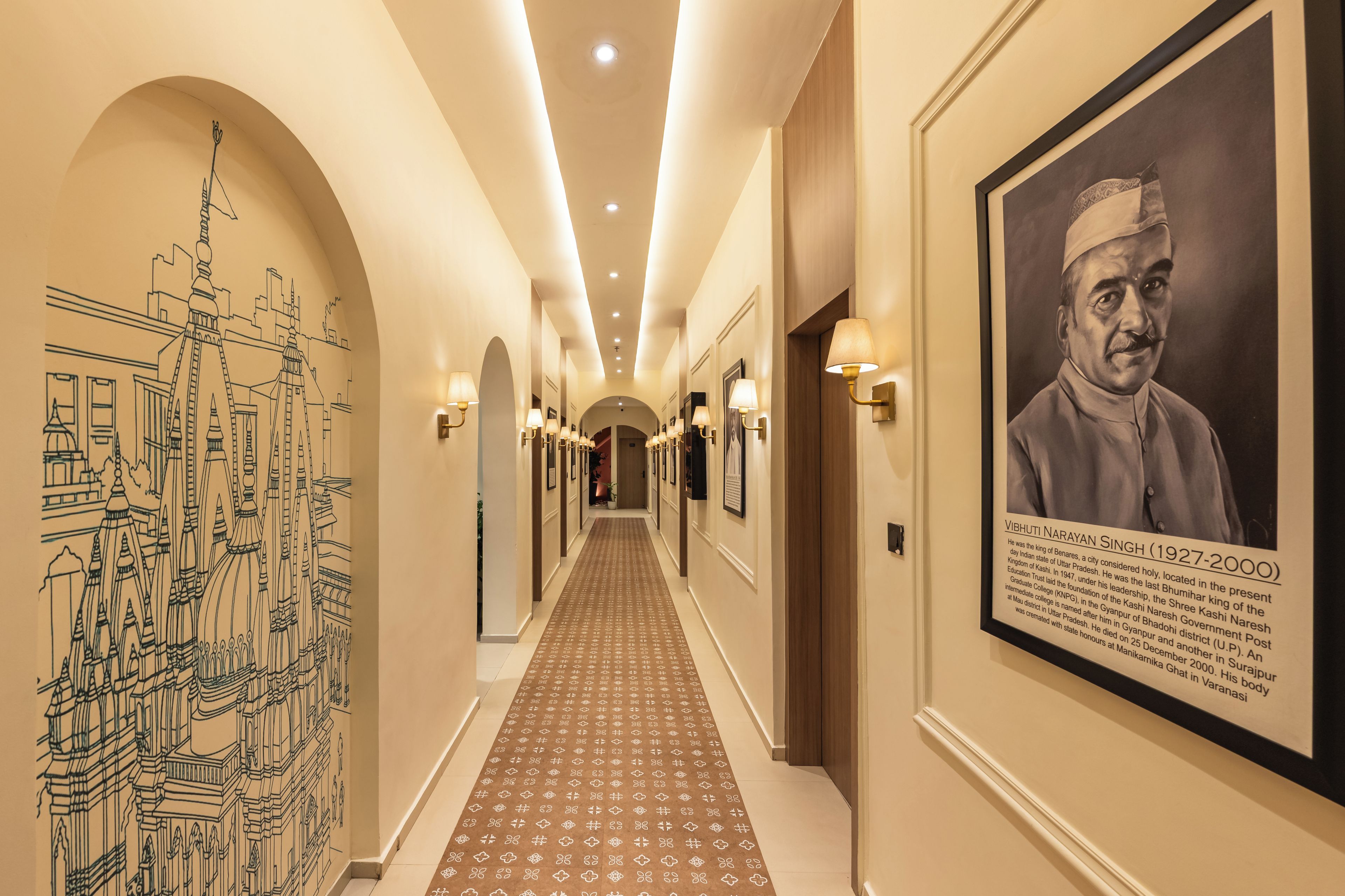 A hotel corridor with a patterned carpet, wall art, and framed photographs.