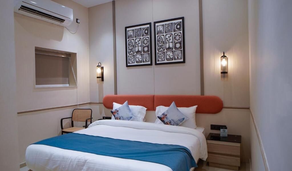 Une chambre d’hôtel comprenant un lit, une table de chevet, une chaise, un climatiseur fixé au mur et deux appliques murales.