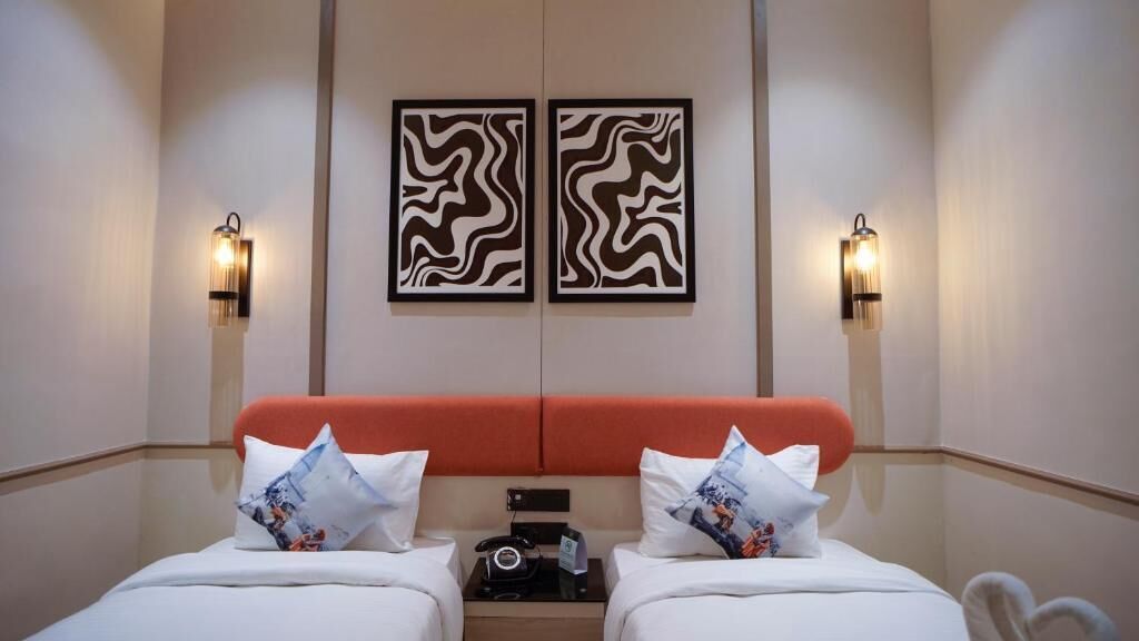 Ein Hotelzimmer mit zwei Betten, einem roten Kopfteil, zwei Wandleuchten und zwei gerahmten abstrakten Kunstwerken.