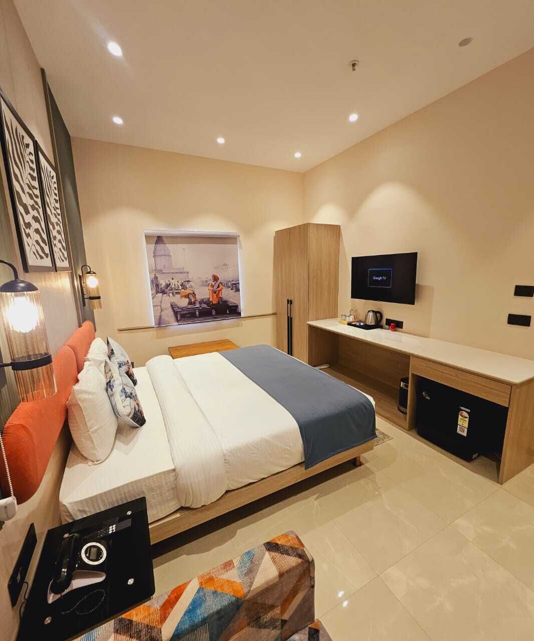 Une chambre d’hôtel moderne, équipée d’un lit, d’un bureau, d’une télévision et ornée d’œuvres d’art au mur.