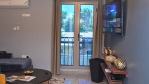 Una sala de estar moderna con una mesa de centro redonda, un sofá, un televisor montado en la pared y un ventanal corredero que da a un balcón exterior.