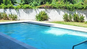 Una piscina rectangular con agua azul cristalina, rodeada por una plataforma de concreto y un bajo muro de piedra con vegetación.