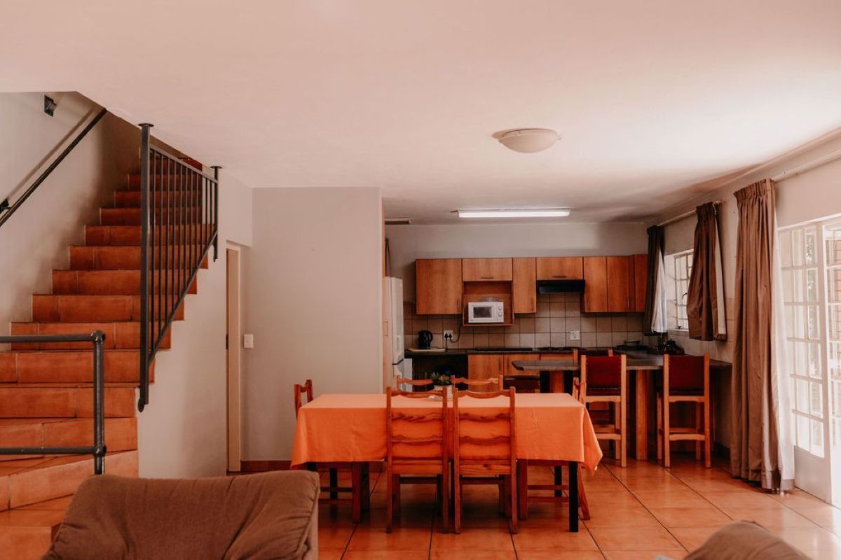 A compact living space with a staircase, a dining area with orange chairs, and a kitchen with wooden cabinets.