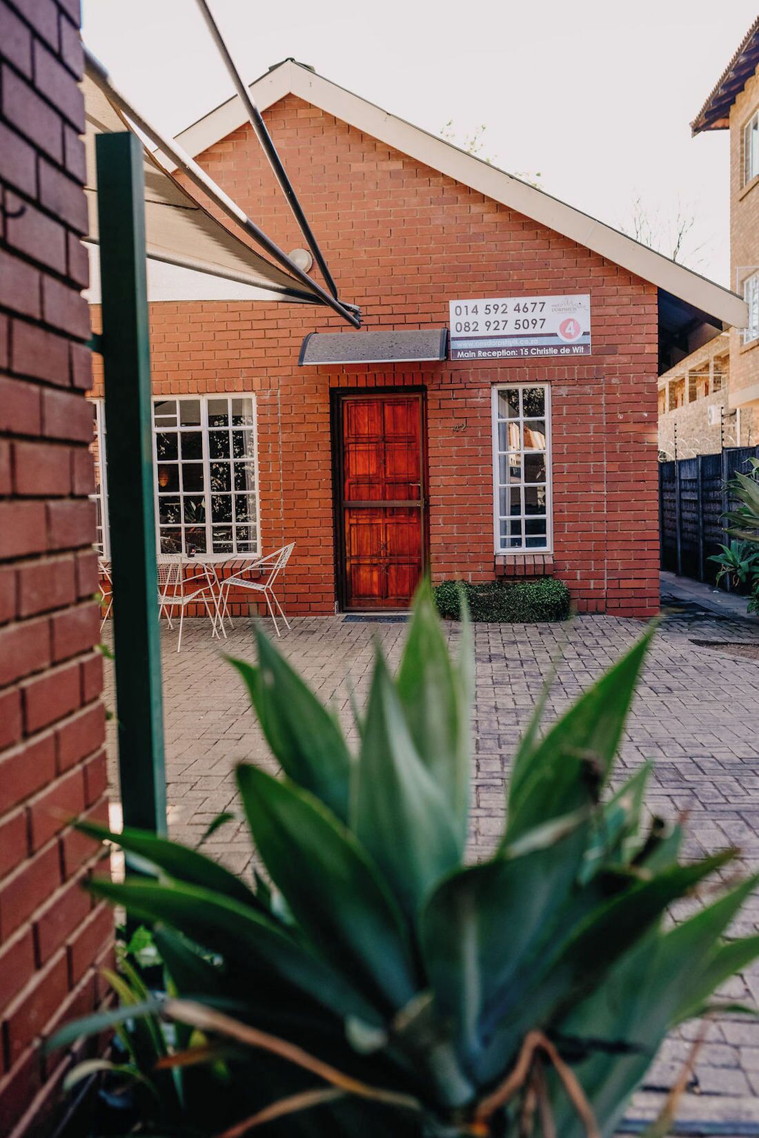 A brick building with a red door and a sign displaying contact numbers.