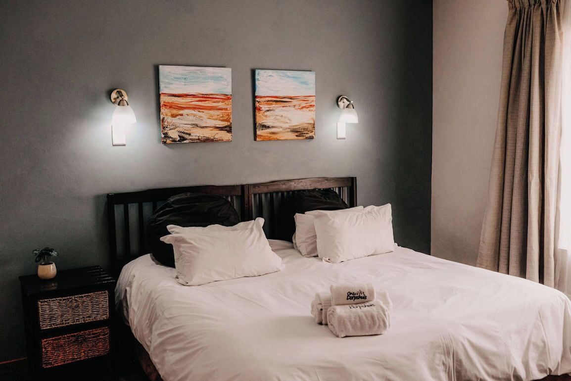Una cama bien tendida con sábanas blancas, dos lámparas de pared y dos cuadros colgados encima.