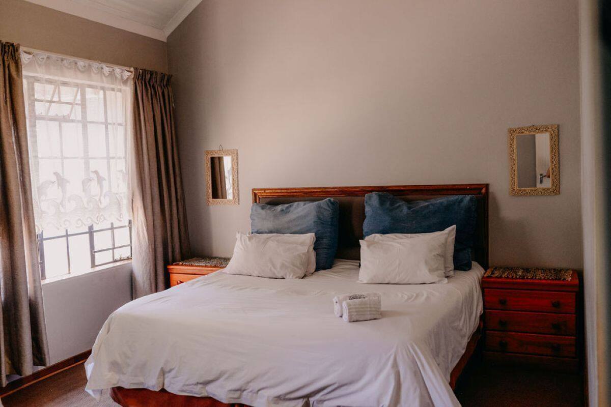 A neatly made bed with white and blue pillows, a wooden headboard, and a red nightstand with drawers.