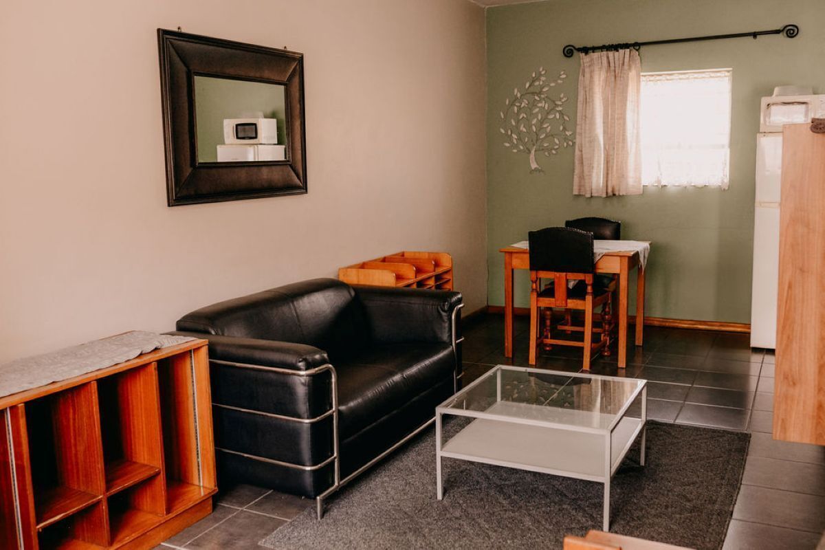 Uma sala de estar com um sofá de couro preto, uma mesa de centro de vidro e uma mesinha lateral de madeira.