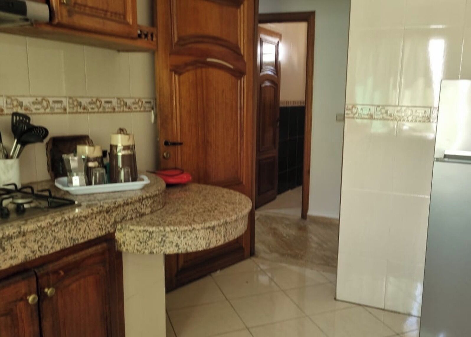 A kitchen with granite countertops, wooden cabinets, a gas stove, and a refrigerator.