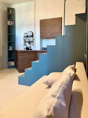 Un interno moderno con un divano beige, una scala con gradini blu, un mobile in legno e una libreria con libri e oggetti decorativi.