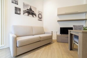A living room with a beige sofa, a flat-screen TV, a wooden coffee table, and wall art including the Eiffel Tower. - Beautiful apartment 1BR/4P – At the Gates of Milan (Sesto San Giovanni)