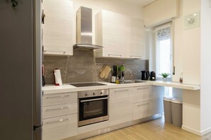 A modern kitchen with a stainless steel range hood, a built-in oven, a sink, and a window with a decorative curtain. - Beautiful apartment 1BR/4P – At the Gates of Milan (Sesto San Giovanni)