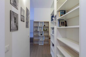A hallway with a wooden bookshelf, a white wall, and a door at the end. - Beautiful apartment 1BR/4P – At the Gates of Milan (Sesto San Giovanni)