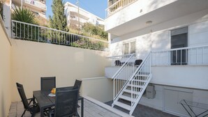 En hyggelig udendørs patio med et bord og stole, en hvid trappe og udsigt til omkringliggende bygninger.