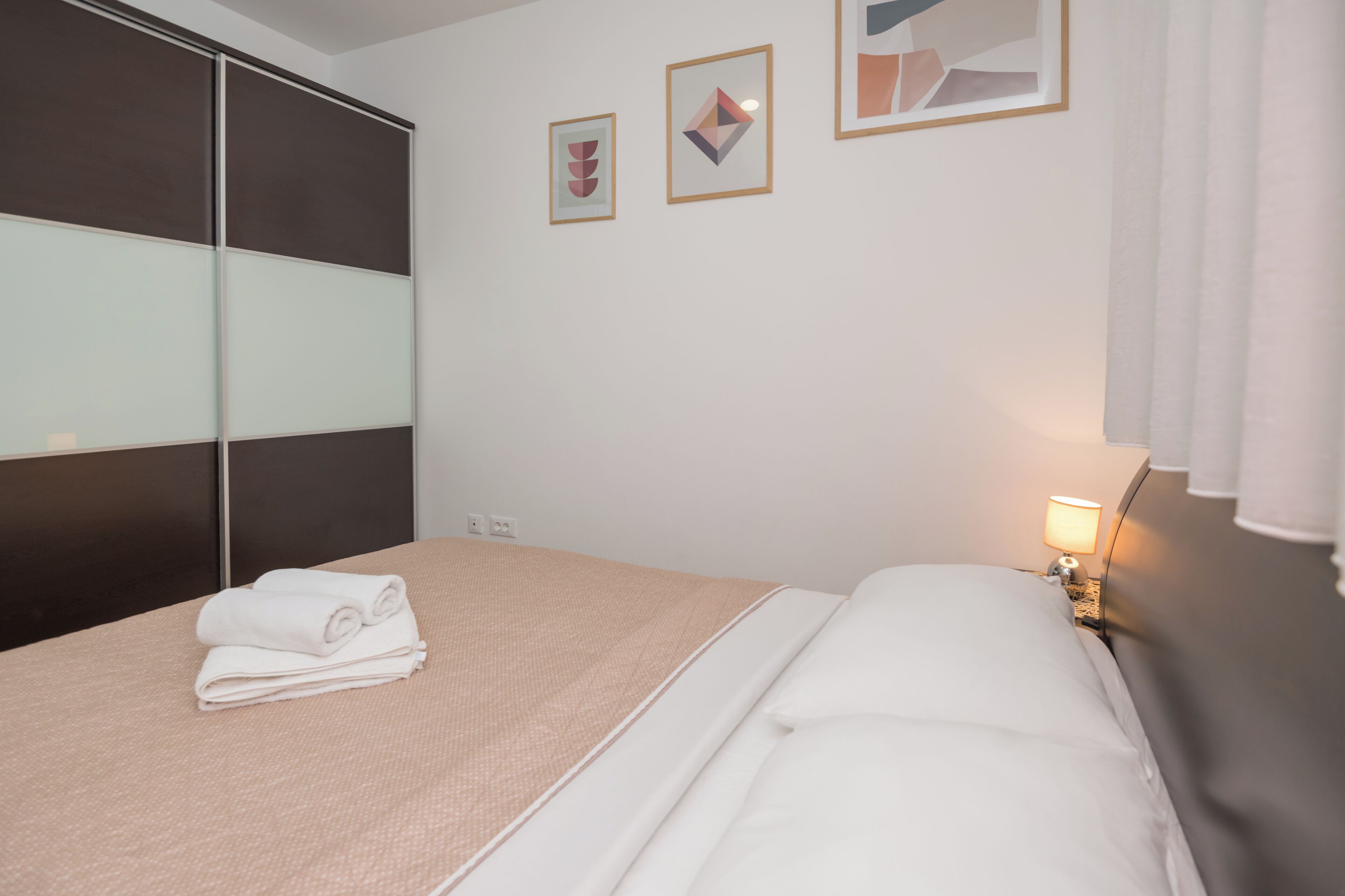 Een hotelkamer met een bed, een nachtkastje, een lamp en twee ingelijste kunstwerken aan de muur.