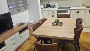 Et moderne køkken med lyse skabe, en emhætte i rustfrit stål og et spiseområde med et træbord og brune stole.