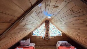 A cozy attic bedroom with two beds, wooden walls, and a sloped ceiling.