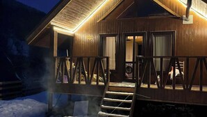A wooden cabin with a covered porch and a fire pit in the snow.