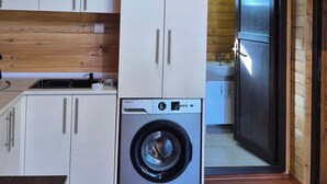 A compact kitchen with white cabinets, a washing machine, and a wooden ceiling.