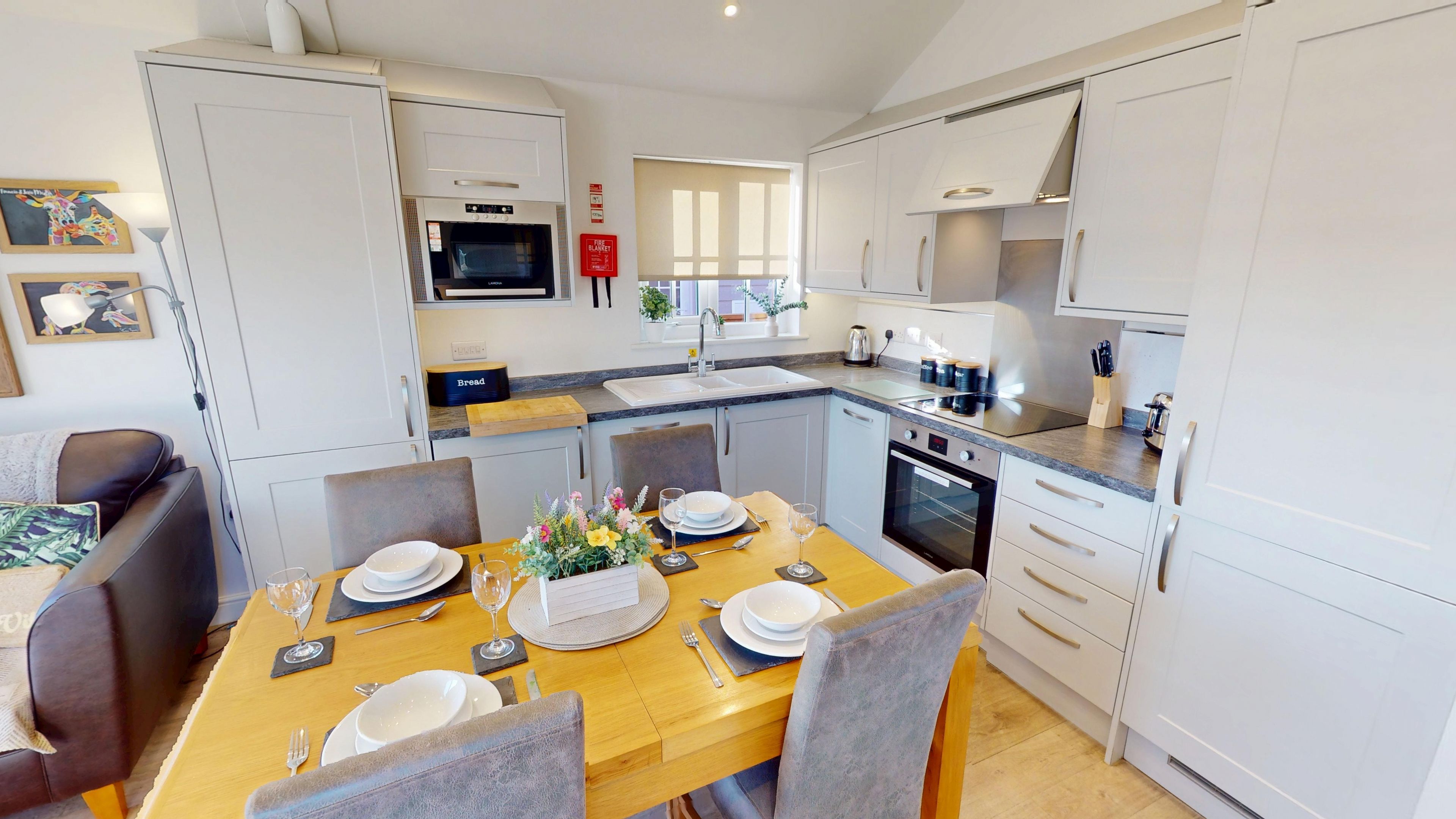 A modern kitchen with white cabinetry, a dining table set for four, and a built-in oven.