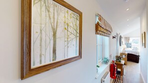 A hallway with a large framed artwork of trees, a window with a view, and a fire extinguisher mounted on the wall. - A luxury 2 bed lakeside lodge that sleeps 4 guests  in 2 bedrooms (Filey)