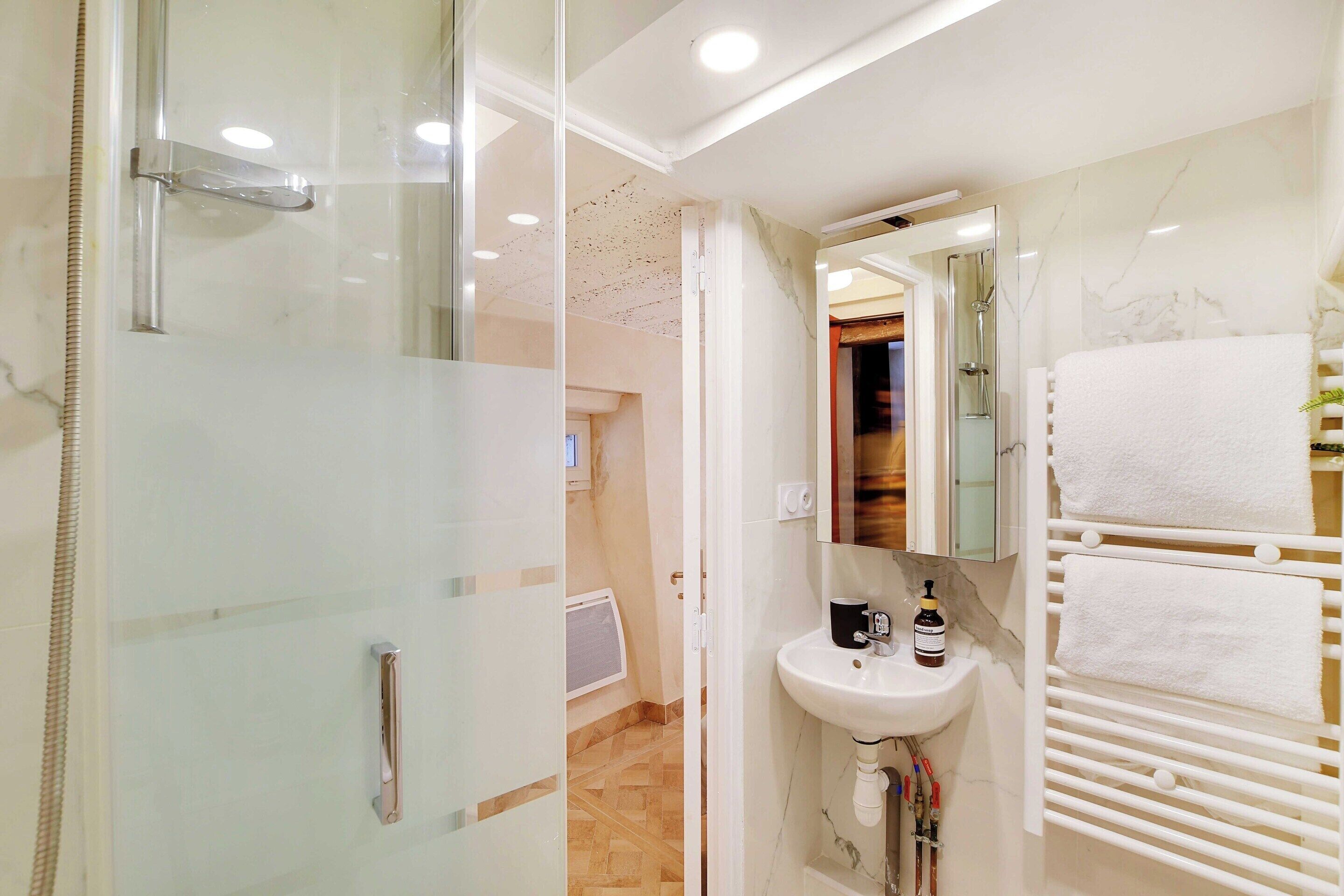 Une salle de bain moderne avec une douche à l’italienne en verre, un lavabo blanc et un porte-serviettes.
