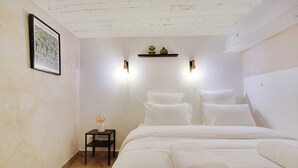 Un dormitorio ordenado con cama, almohadas, una mesita de noche con lámpara y un cuadro en la pared.