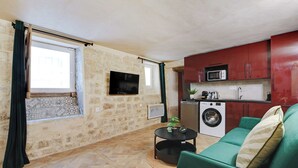 Un espacio habitable compacto con sofá, lavadora y televisor montado en la pared.