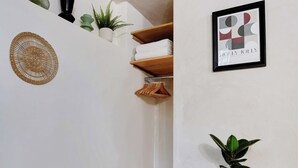 Un pasillo con suelo de espiga, un estante negro con una cesta tejida, un cuadro en la pared y una planta en maceta sobre una mesita.