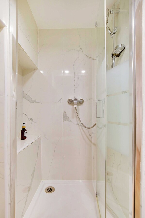 A glass-enclosed shower with a marble wall, a handheld showerhead, and a handheld faucet. - Charming Appt- 4p/1br- in the Heart of the Marais (Paris)