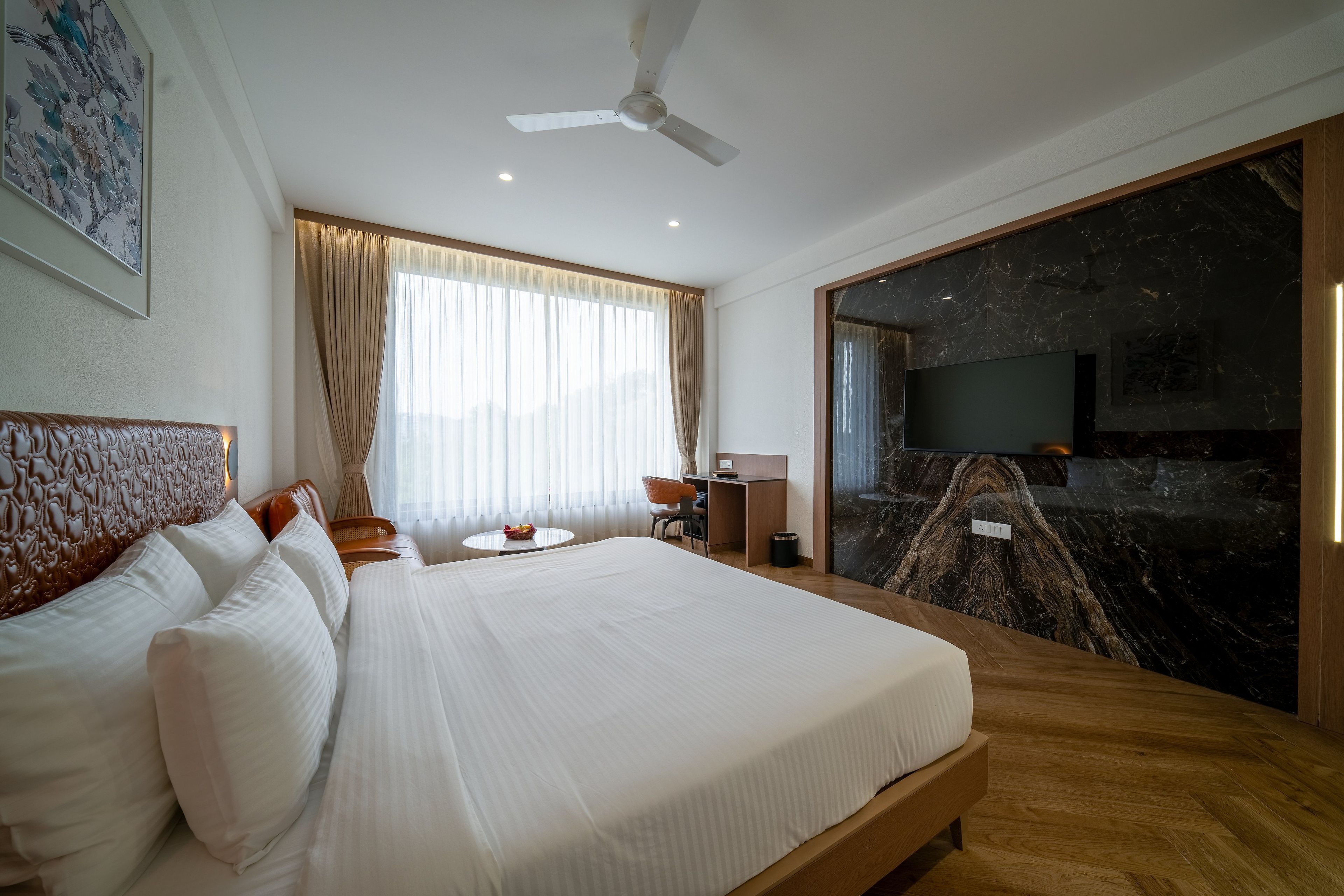 Een hotelkamer met een groot bed, een bureau, een stoel, een plafondventilator en een marmeren wand.