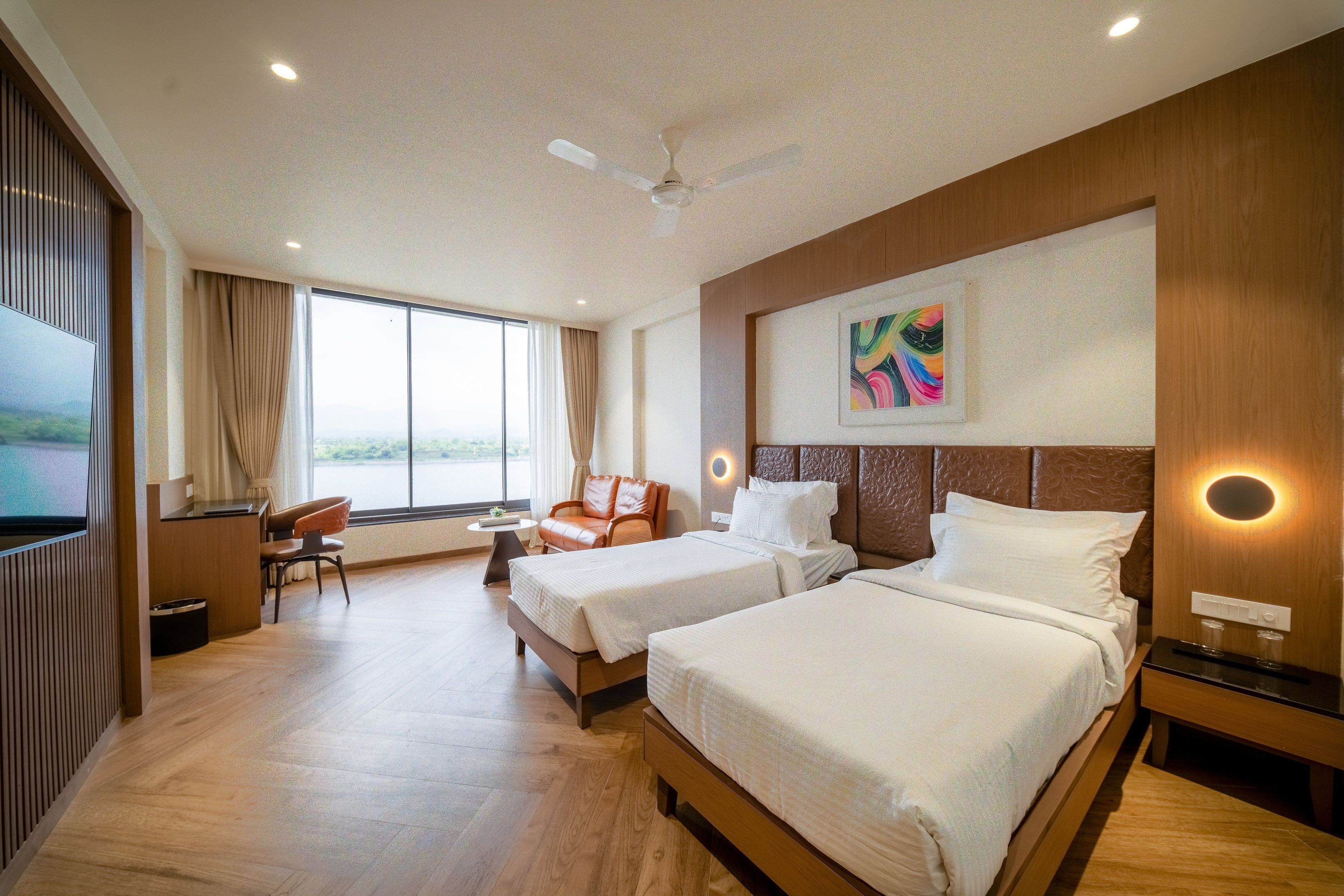 A hotel room with two beds, a desk, a chair, and a large window.