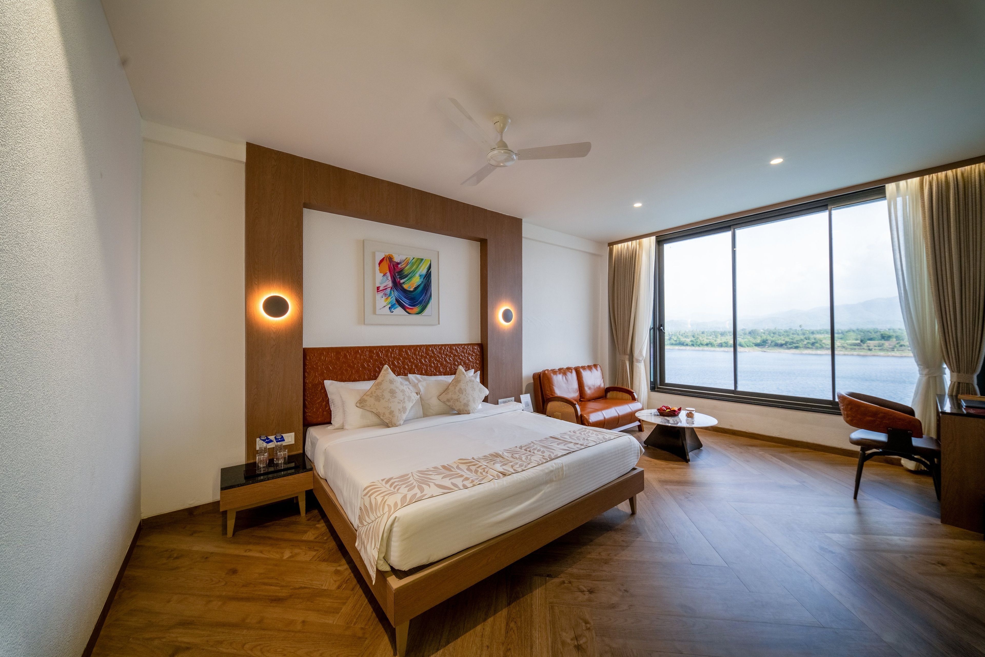 A hotel room with a large bed, a desk, a chair, a view of the outdoors, and a ceiling fan.