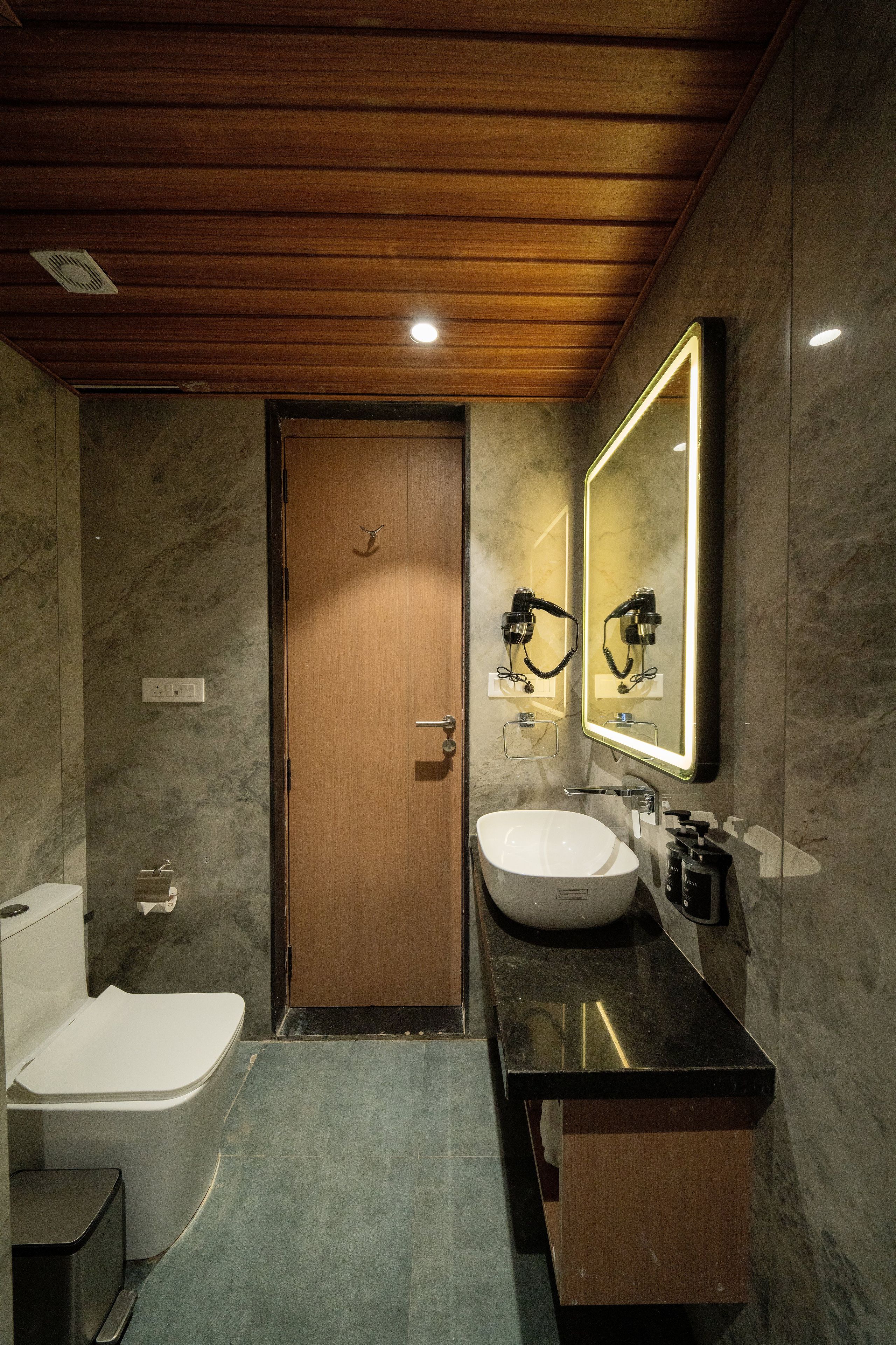Ein modernes Badezimmer mit Holzboden, einem großen Spiegel, einem weißen Waschbecken und einer Toilette.