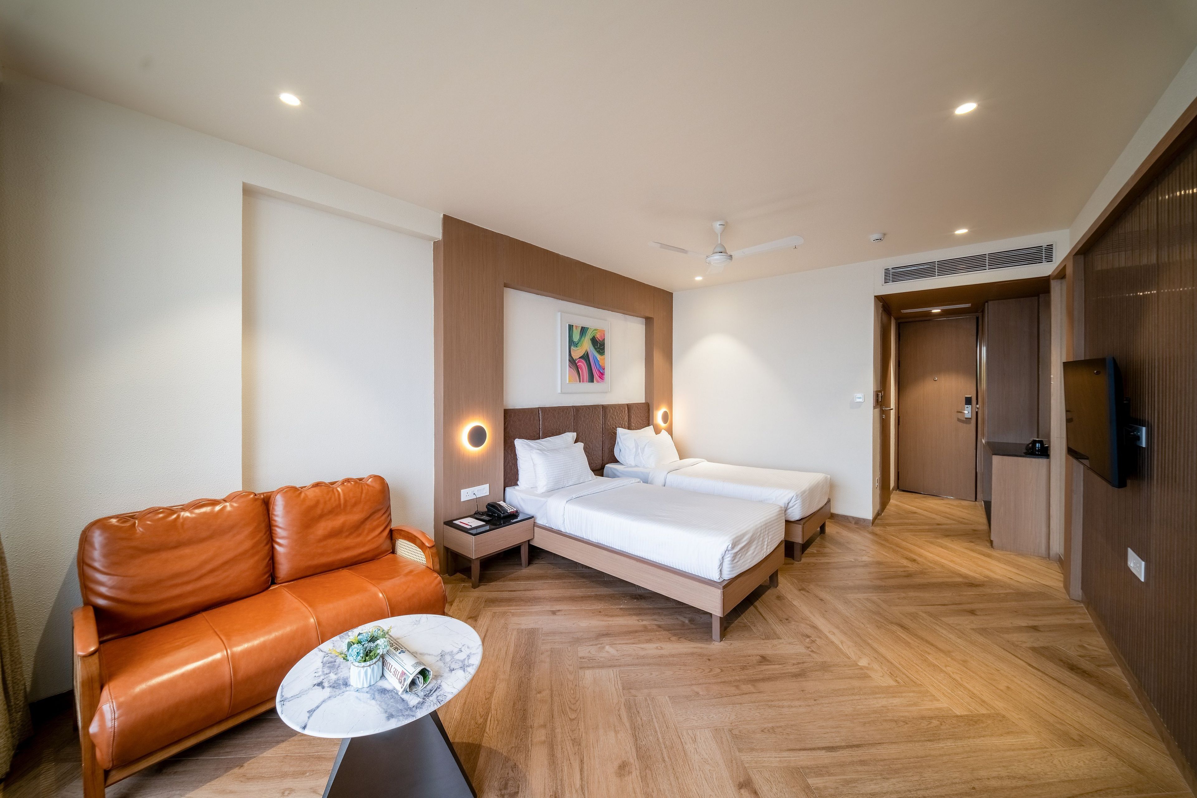 Een hotelkamer met een bank, twee bedden, een klein tafeltje en een plafondventilator.